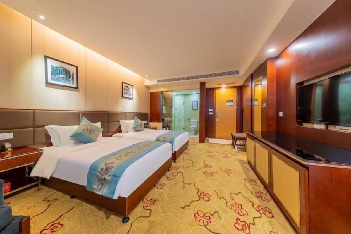 A hotel room with two beds, a TV, and a carpeted floor.