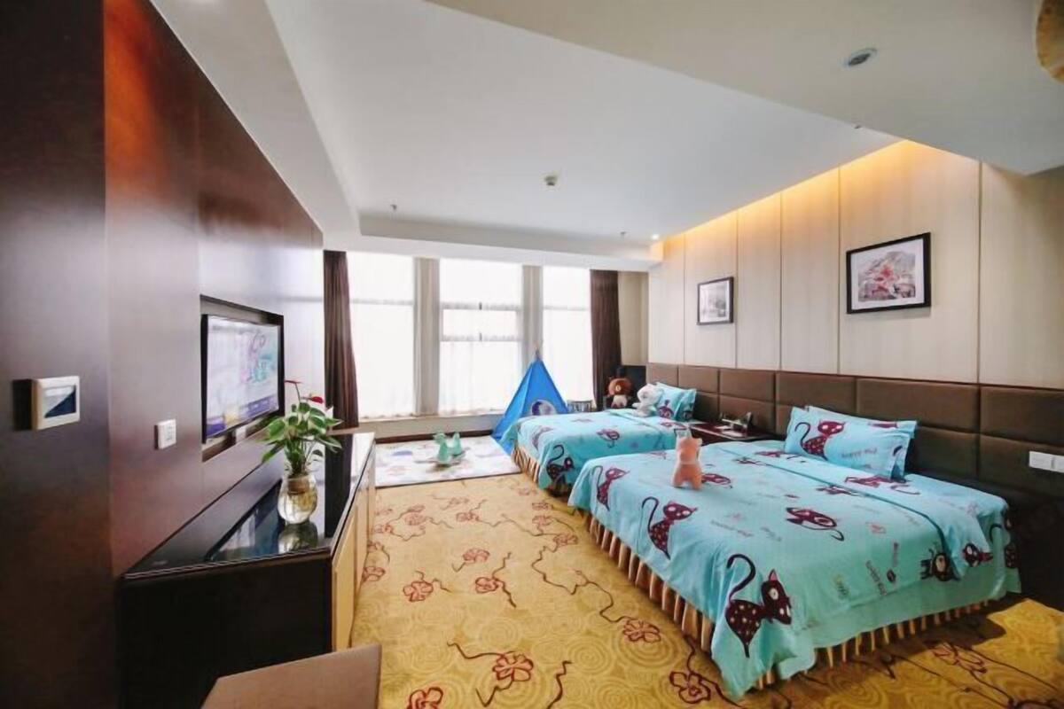 A hotel room with two beds, a desk, a chair, a TV, and a window with curtains.