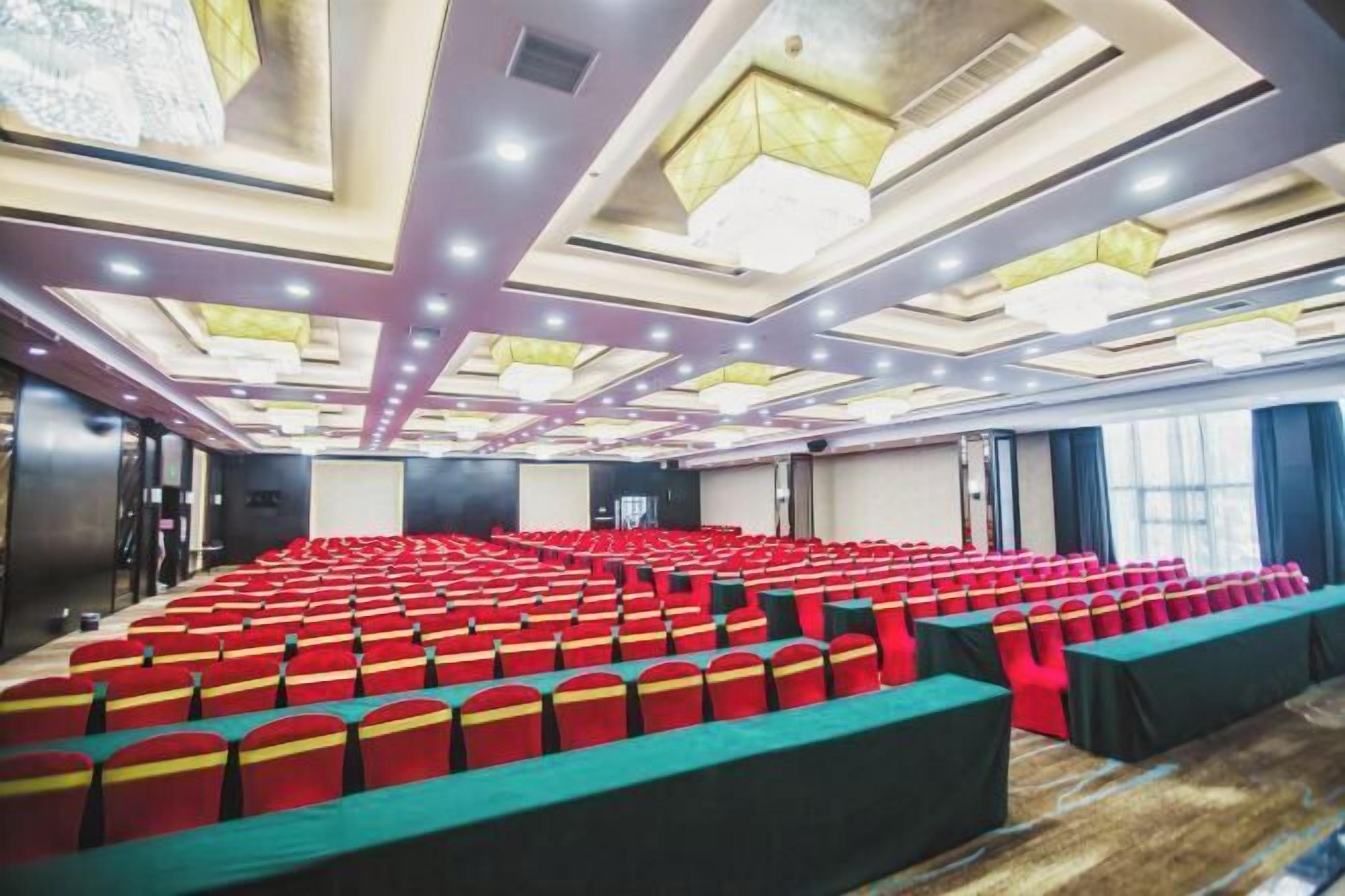 A conference room with rows of red chairs and a long table, equipped with ceiling lights and a modern design.
