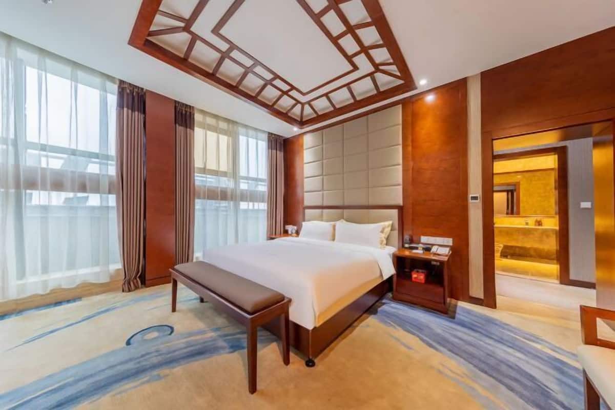 A hotel room with a large bed, a bench, a nightstand, and a mirror.