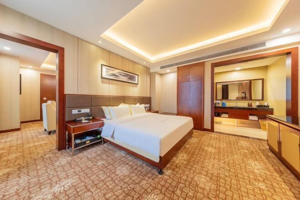 A hotel room with a bed, bedside table, lamp, and a large mirror.