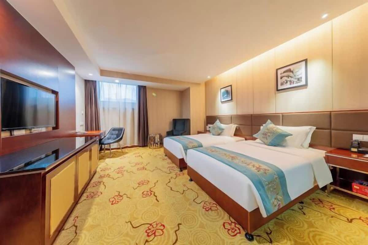 A hotel room with two beds, a desk, a TV, and a chair.