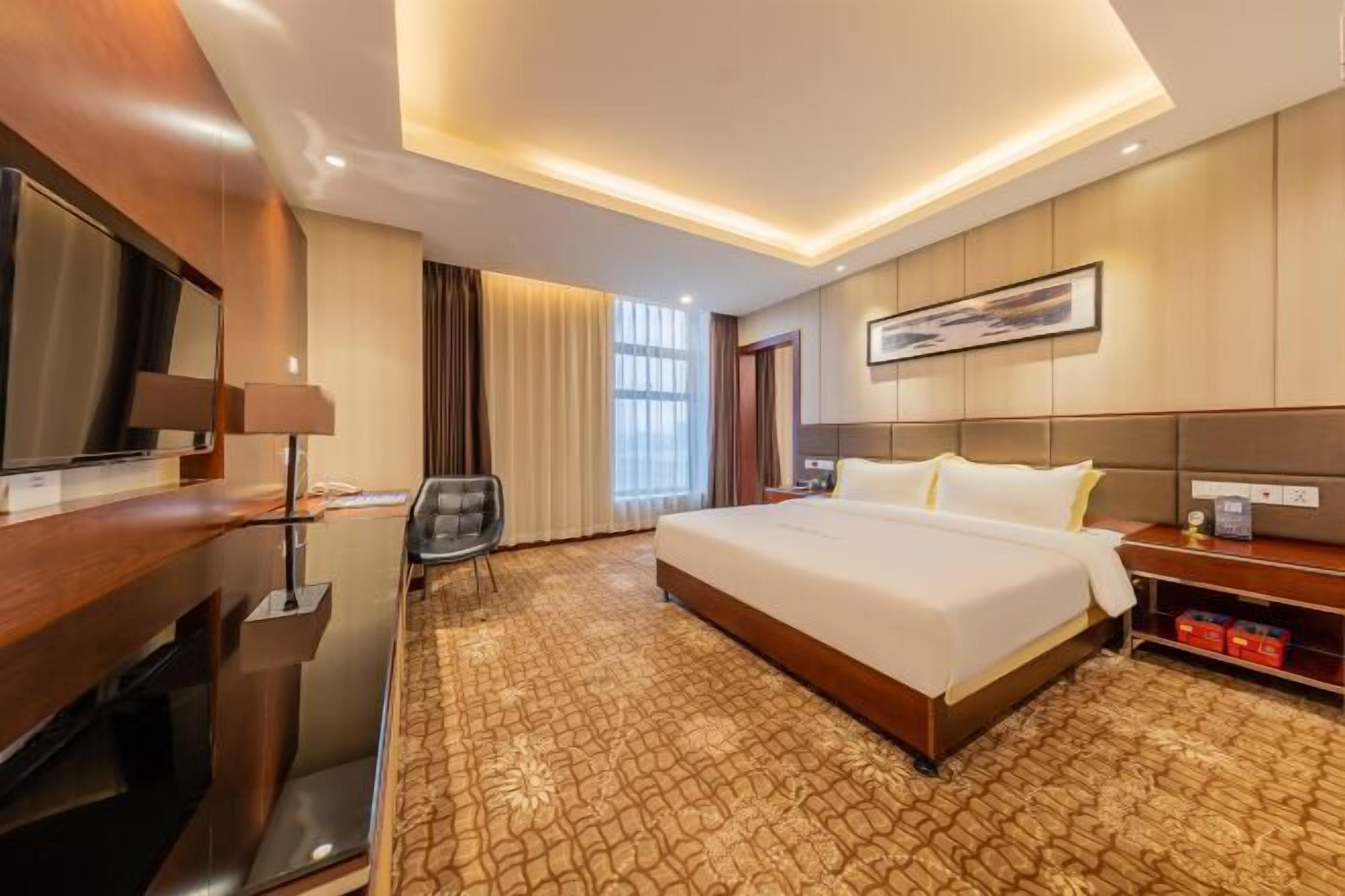 A hotel room with a large bed, a desk with a lamp, a chair, and a television.