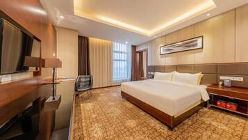 A hotel room with a large bed, a desk with a lamp, a chair, and a television.