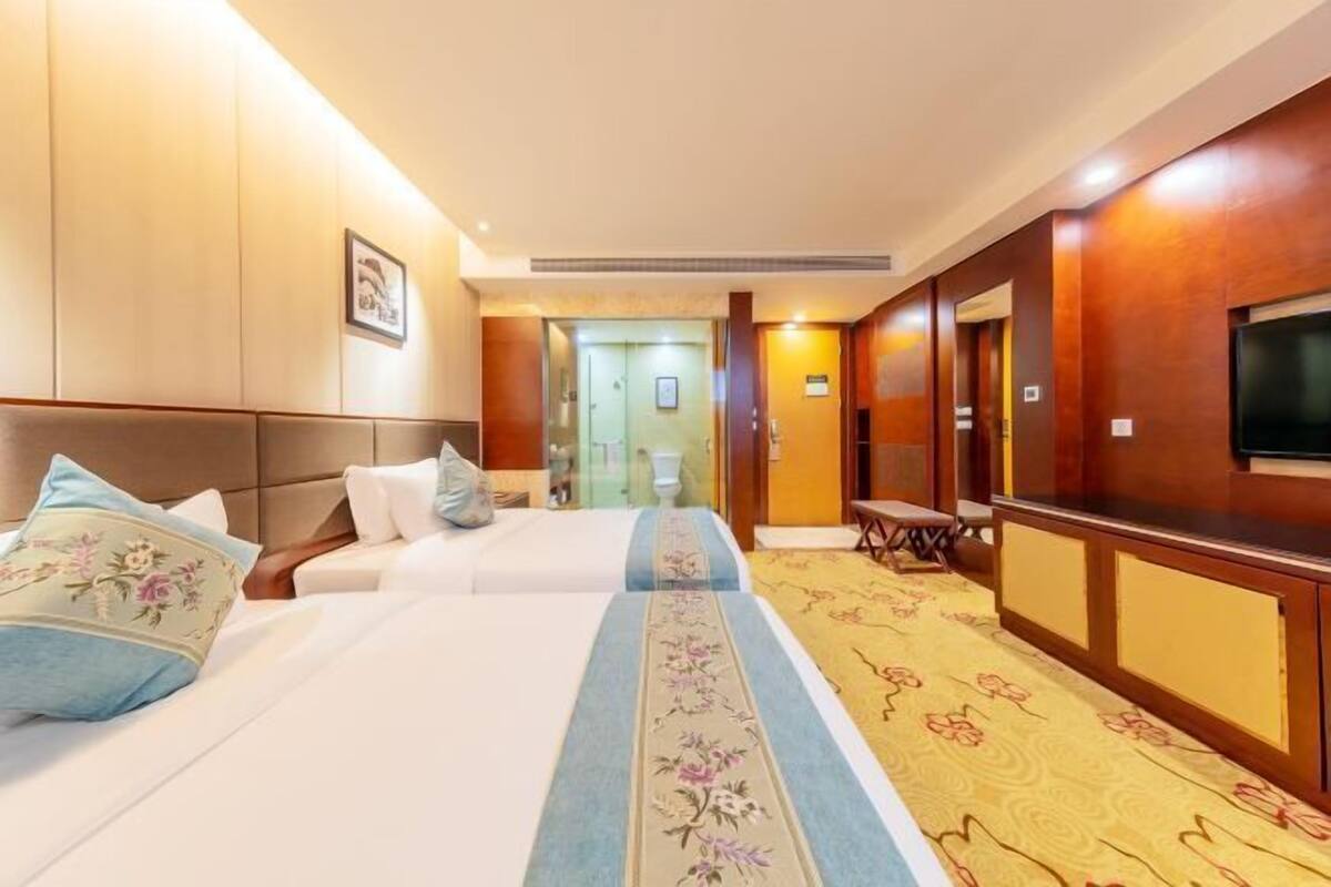 A hotel room with two beds, a TV, a desk, and a carpeted floor.