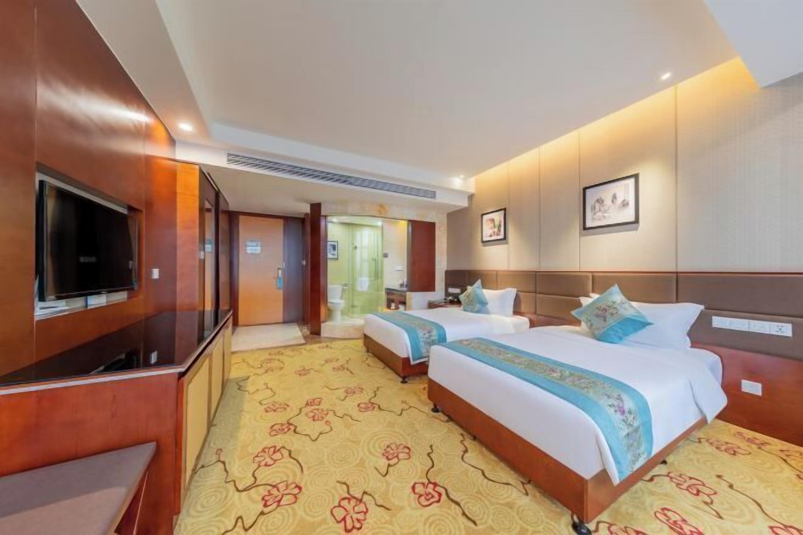 A hotel room with two beds, a TV, a desk, and a bathroom visible through an open door.
