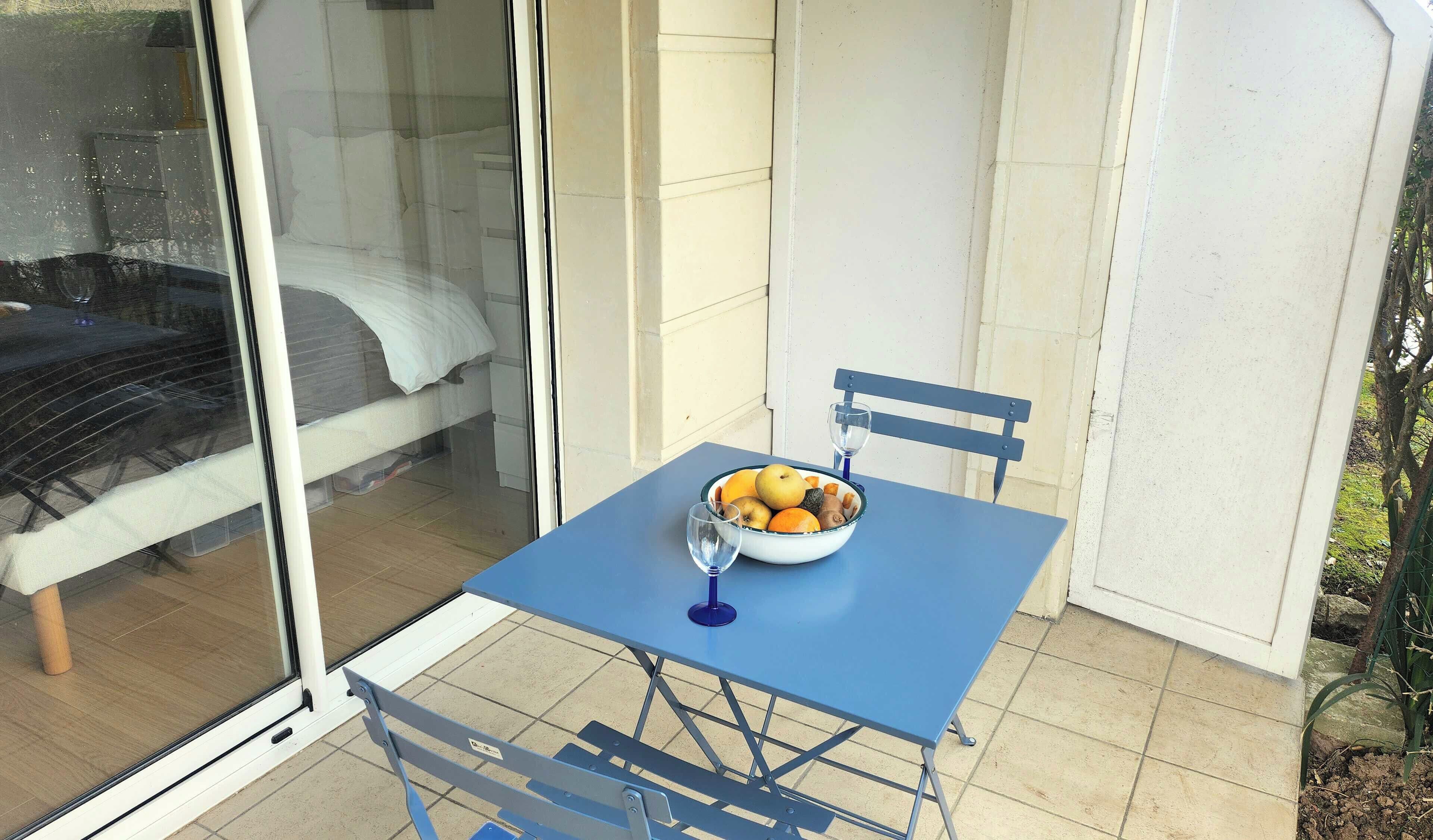 En lille balkon med et bord, en stol og en skål med frugt.