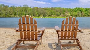 Zwei hölzerne Adirondack-Stühle mit Blick auf einen See und eine bewaldete Uferlinie.