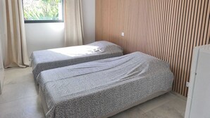 A bedroom with two beds, a window with curtains, and a wooden slatted wall.