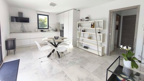 A modern kitchen with white cabinetry, a marble backsplash, and a dining area with a glass table and white chairs.