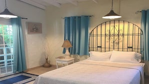 Une chambre à coucher comprenant un lit, une table de chevet, une lampe, un ventilateur de plafond et une fenêtre avec des rideaux.