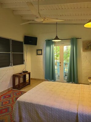 Una camera con un letto, un tavolino, una TV fissata al muro e una finestra con tende.