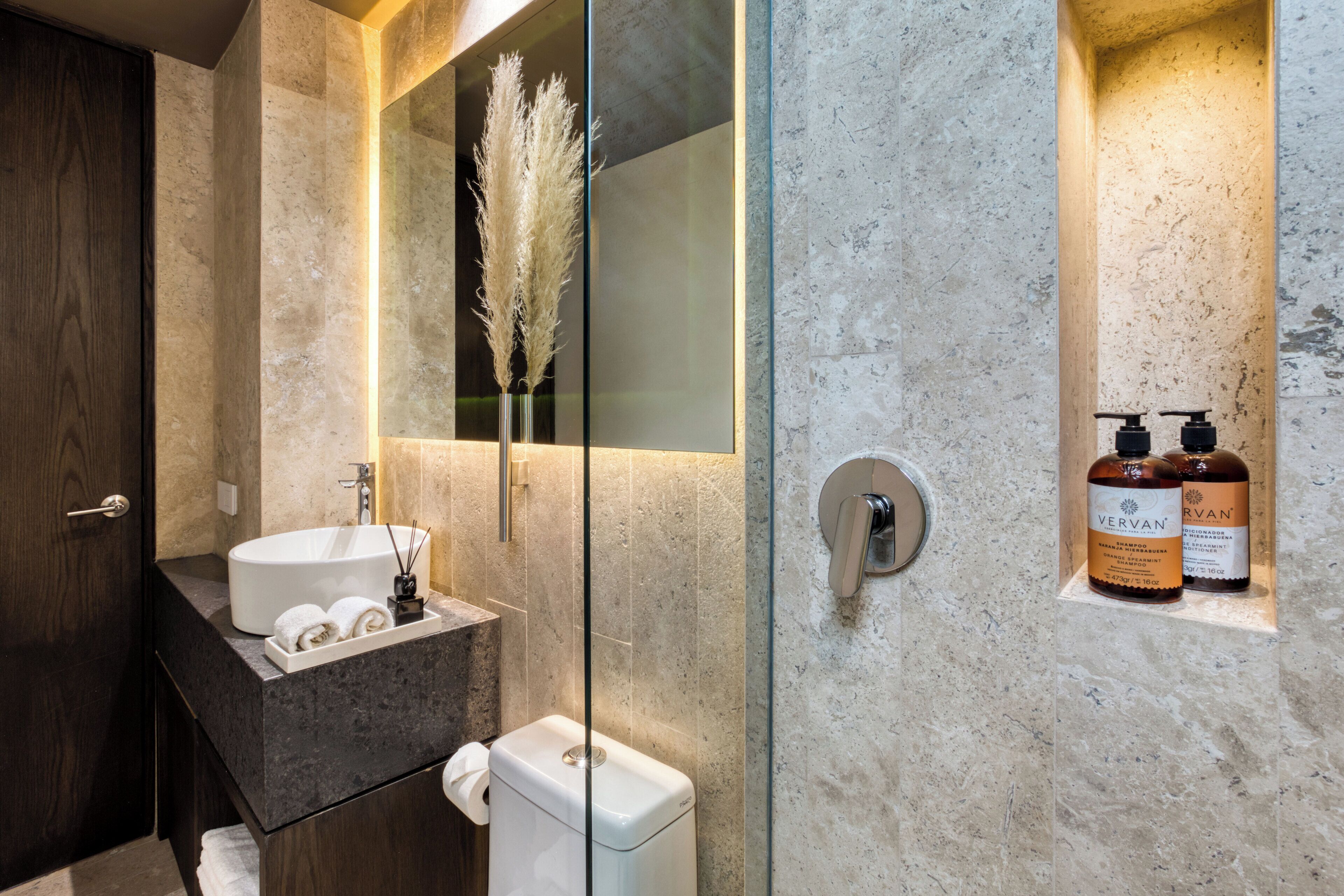 Un baño moderno con lavamanos de mármol, inodoro y cabina de ducha de vidrio.