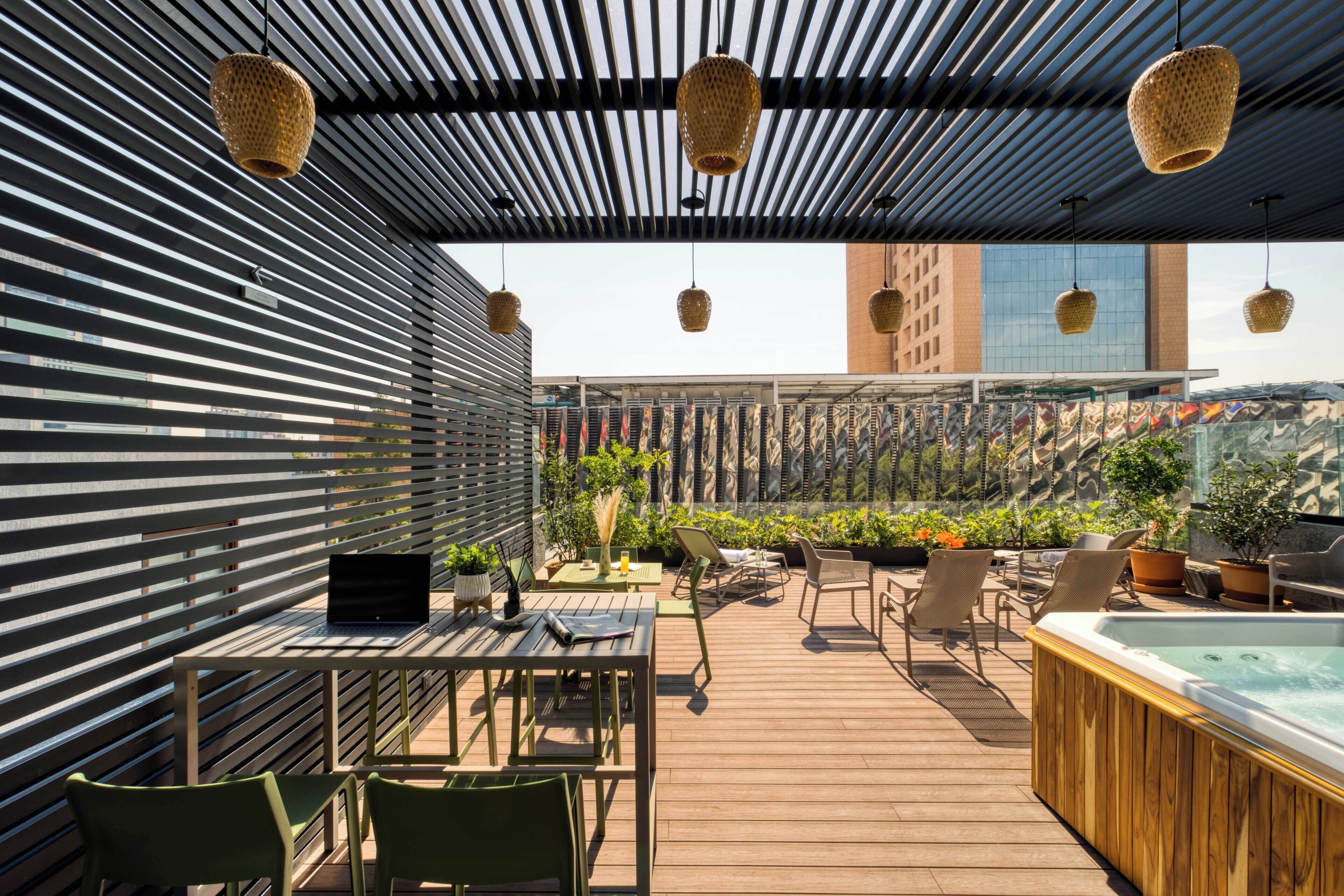 Una terraza en la azotea con cubierta de madera, mobiliario exterior, un jacuzzi y un portátil sobre una mesa.