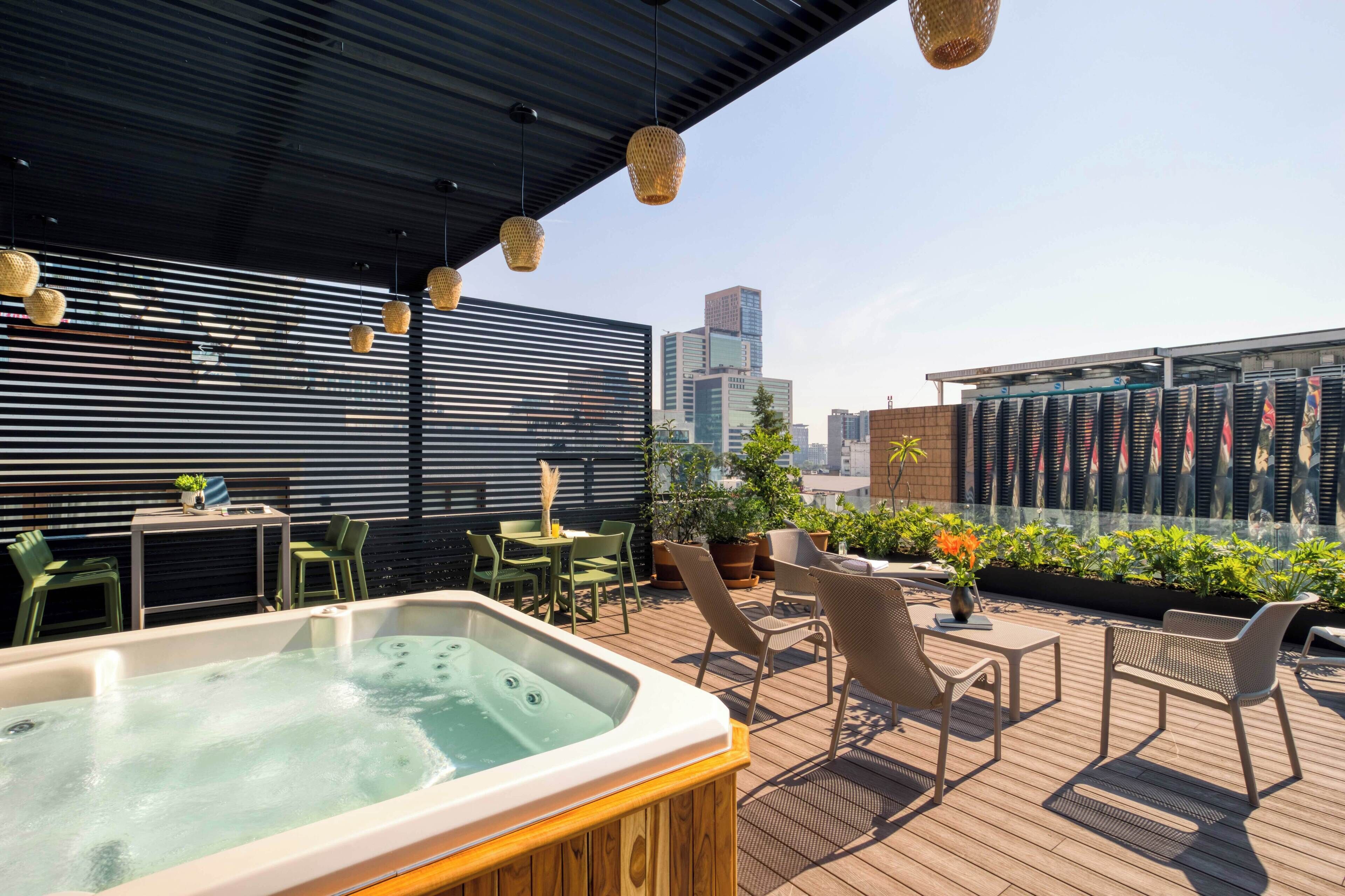 Eine Dachterrasse mit Whirlpool, Sitzgelegenheiten im Freien, Blumentöpfen und Blick auf die Stadtlandschaft.