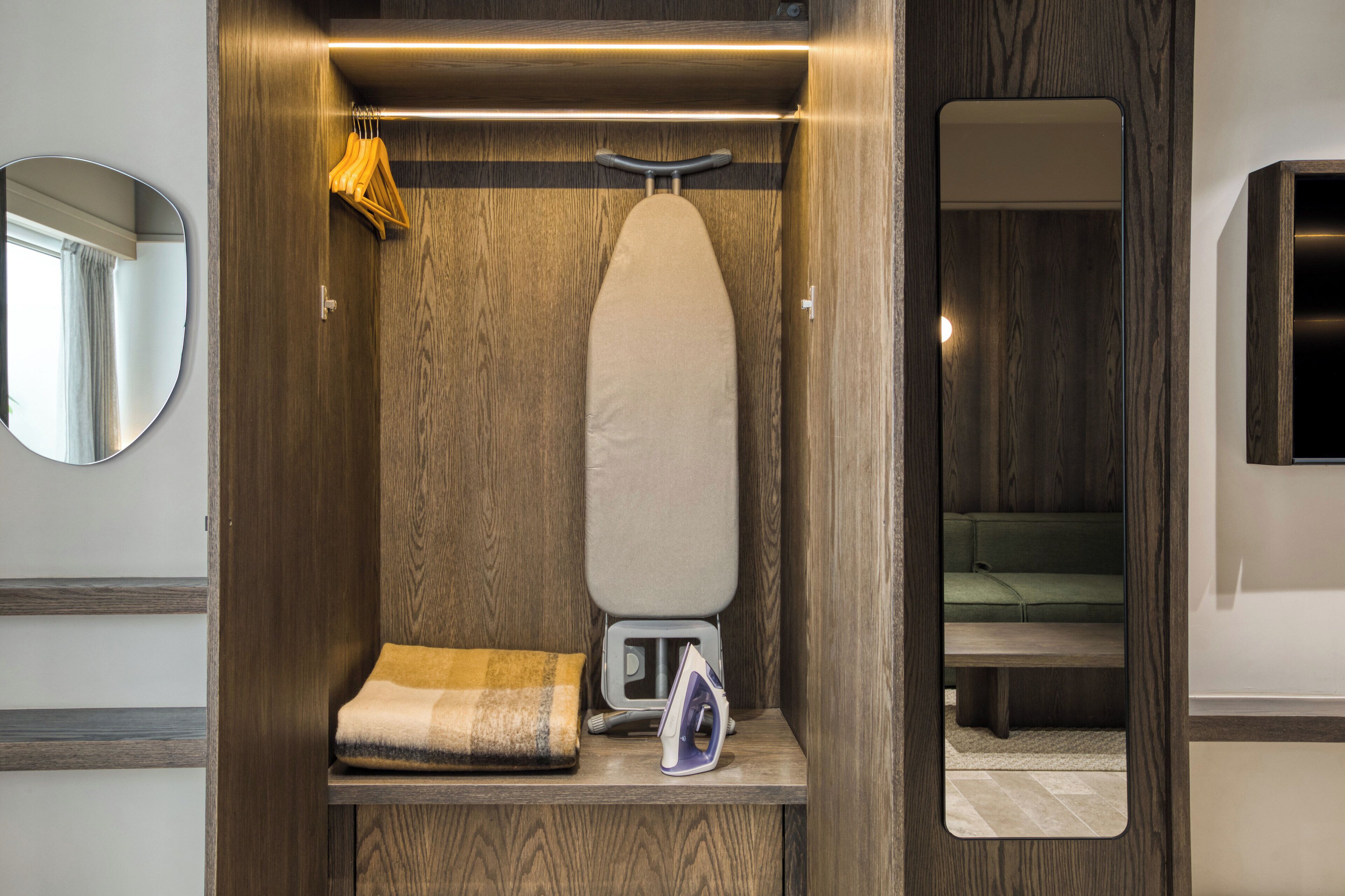 A compact, wood-paneled closet with a hanging iron, an ironing board, and a folded blanket.