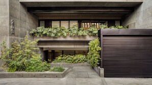 Un edificio moderno con fachada de concreto, un amplio portón de garaje y un pequeño jardín con diversas plantas.