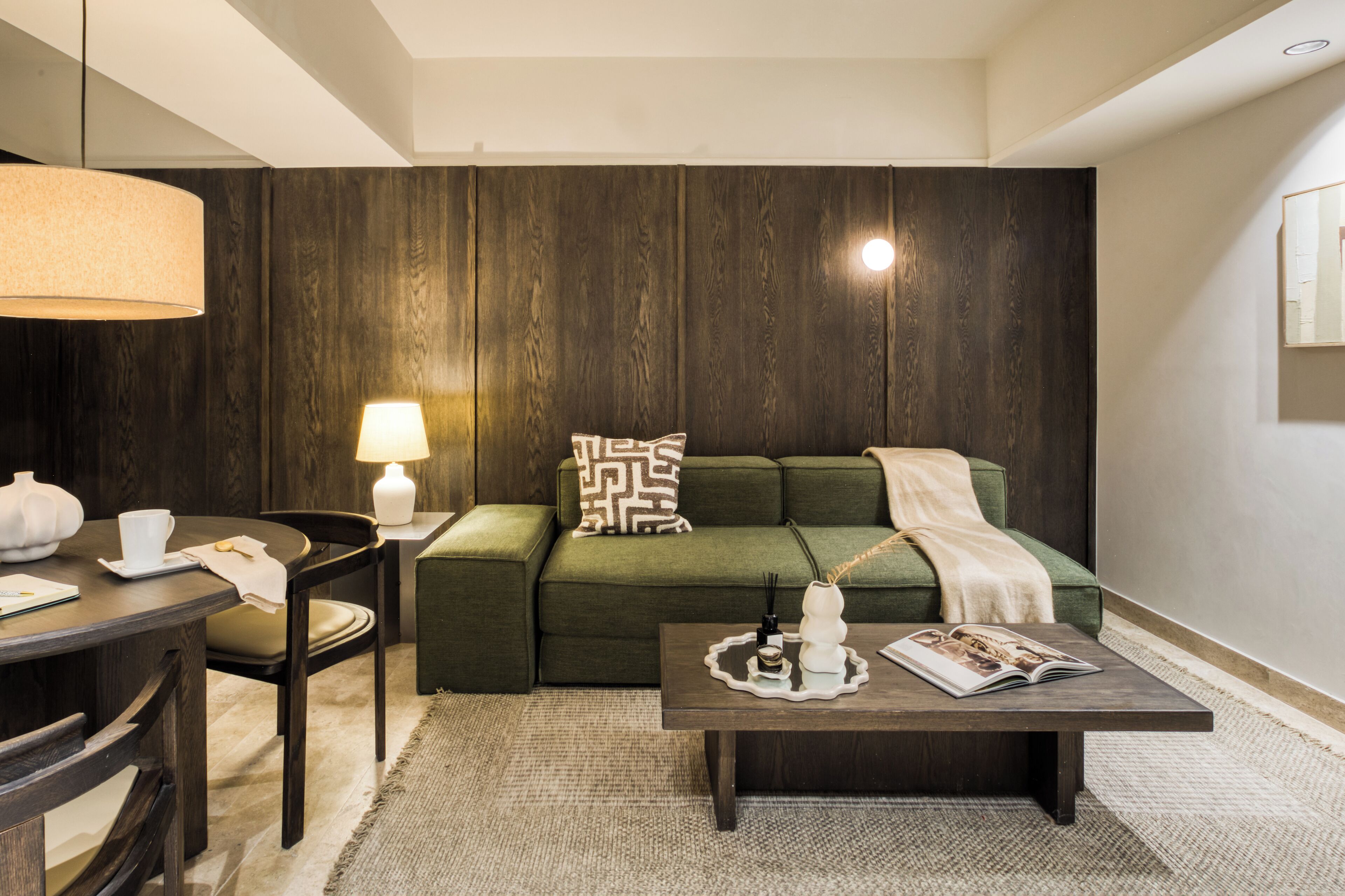 Een moderne woonkamer met een groene bank, een bijzettafeltje met decoratieve objecten, een lamp en een houten accentmuur.