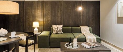 Een moderne woonkamer met een groene bank, een bijzettafeltje met decoratieve objecten, een lamp en een houten accentmuur.