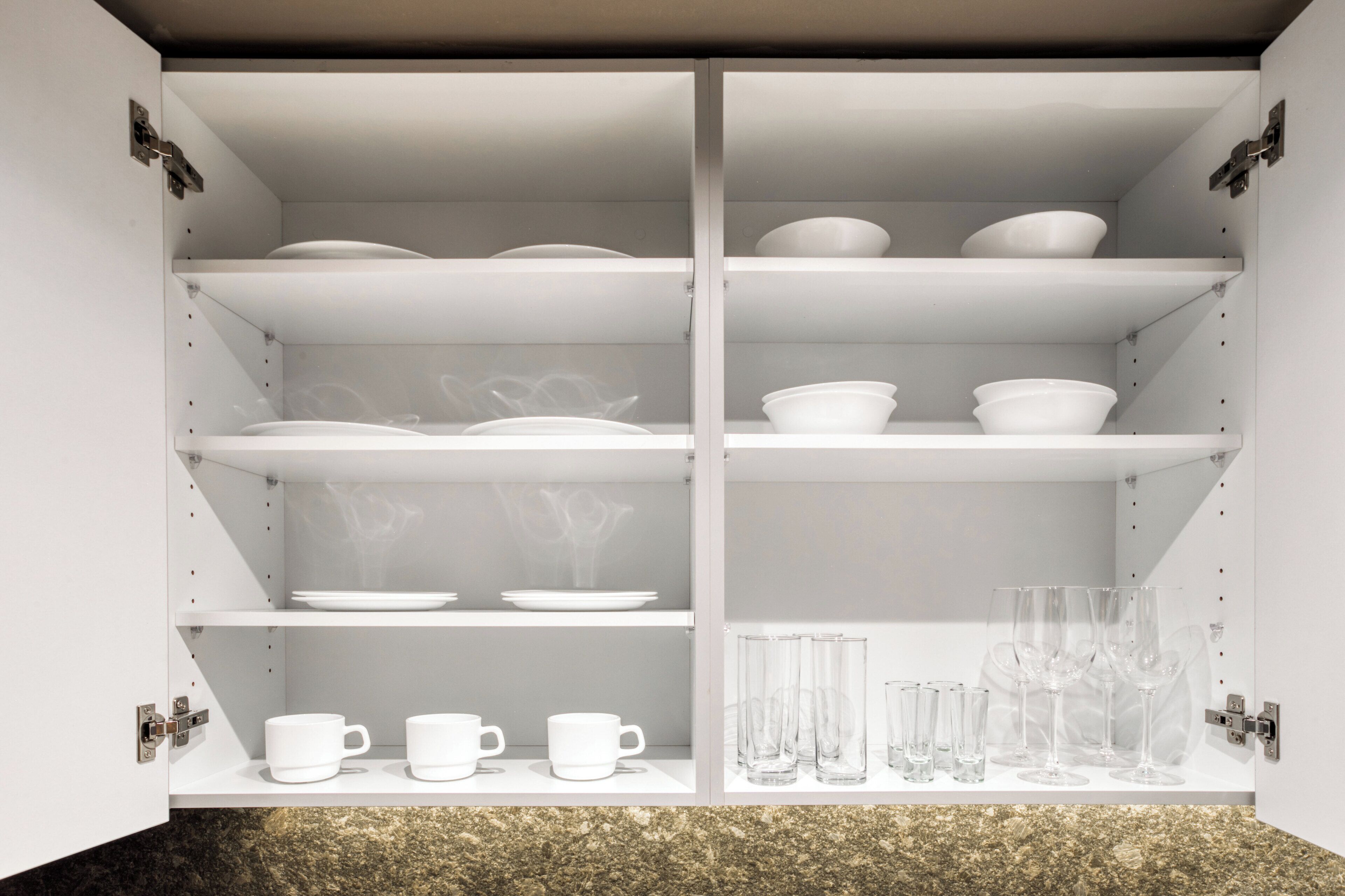 A white cabinet with multiple shelves containing white bowls, plates, and glasses.