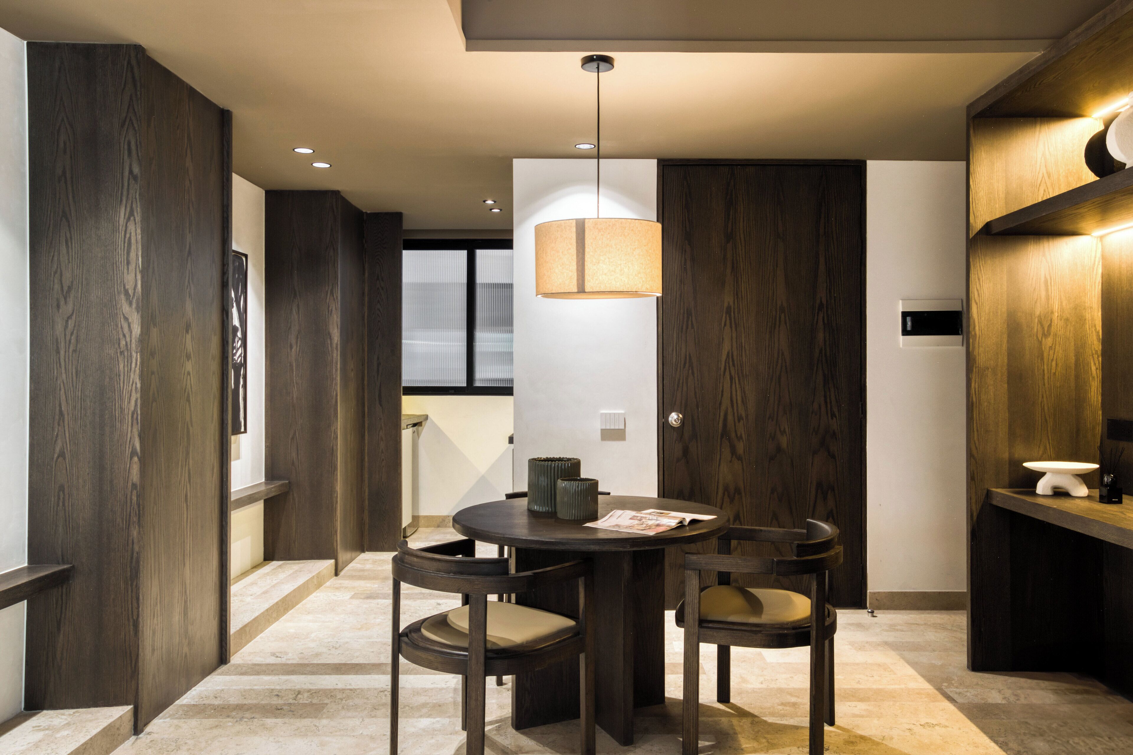 A modern kitchen with dark wood cabinetry, a round dining table with chairs, and a pendant light.