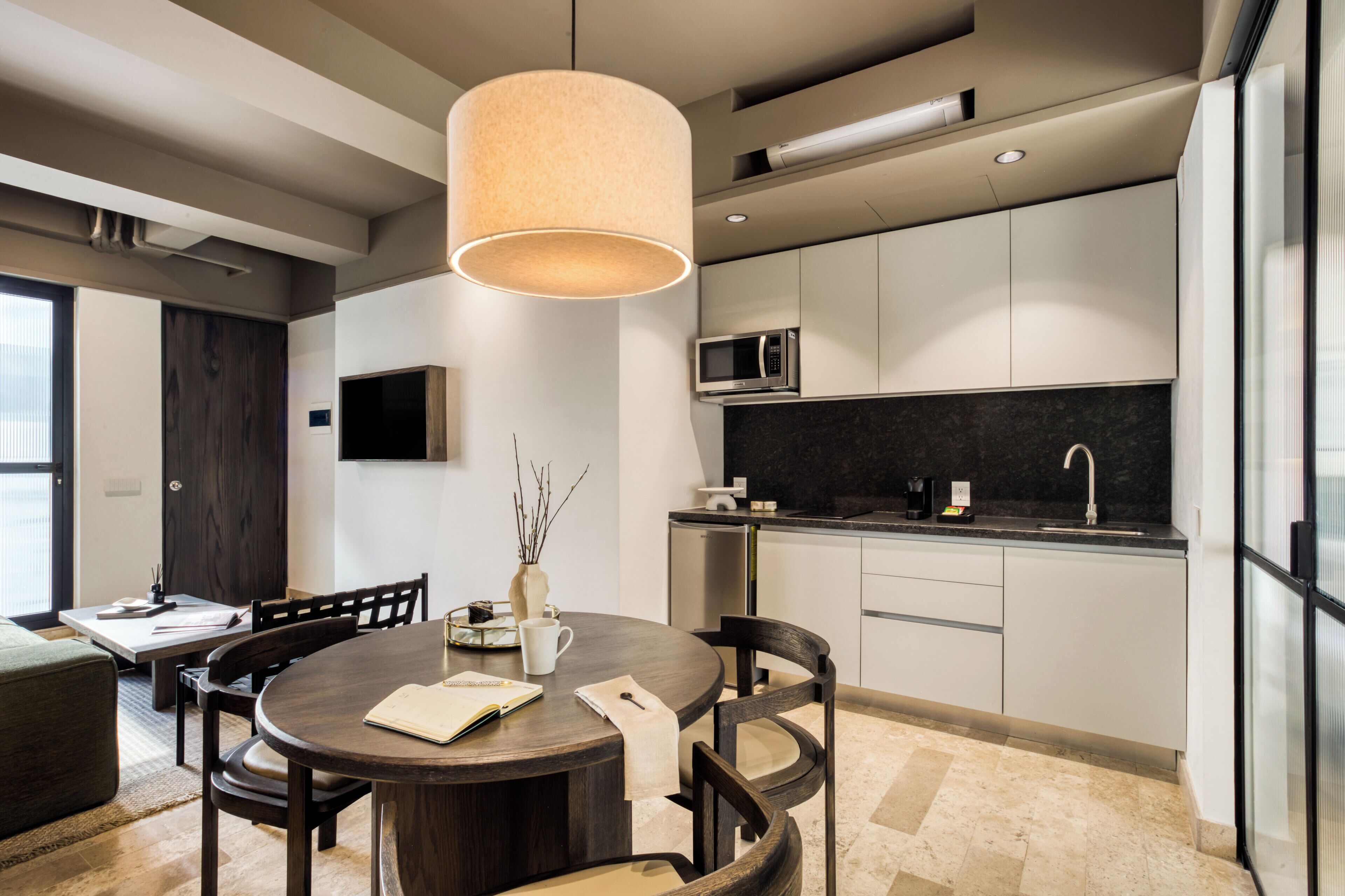Une cuisine moderne avec des meubles blancs, un plan de travail noir et un four à micro-ondes. On y trouve également un coin repas avec une table ronde et des chaises.