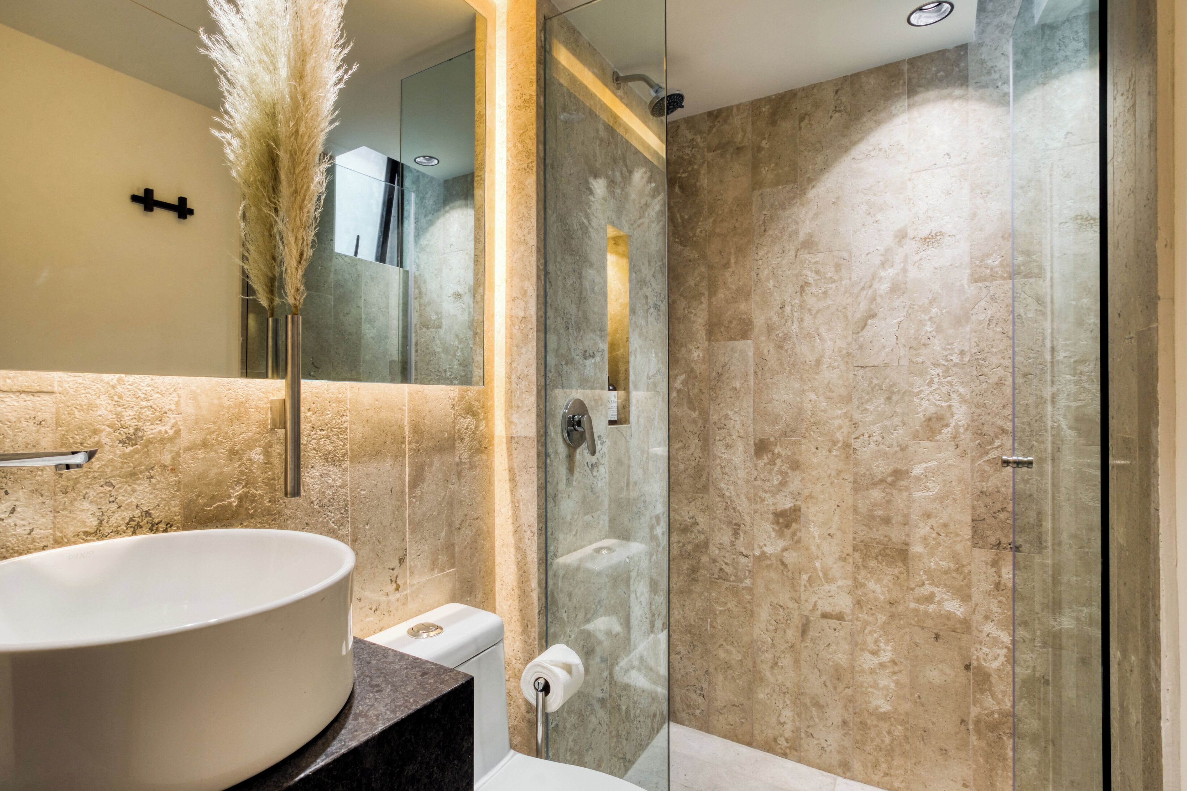 A modern bathroom with a large oval sink, a glass-enclosed shower, and a marble-tiled wall.