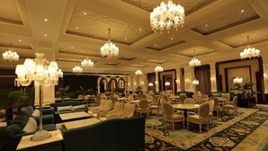Spaziosa hall d'albergo con diverse zone salotto, lampadari e un tappeto decorato.