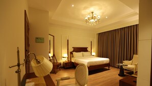 A hotel room with a bed, a chair, a desk, a lamp, and a chandelier. - The Lauriant Resorts (Patiala)