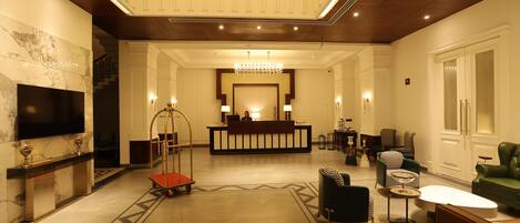 A spacious lobby with a reception desk, a chandelier, and modern seating arrangements.