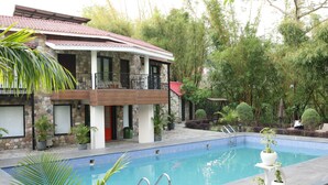 A swimming pool with a stone and wood exterior, surrounded by potted plants and trees. - The Lauriant Resorts (Patiala)