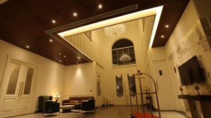 Un'ampia hall con soffitto alto, un lampadario, un'area salotto con divano e poltrone, e un carrello rosso.