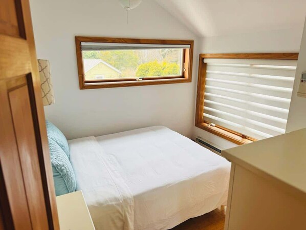 Una habitación pequeña y bien iluminada con una cama individual, una ventana con persianas y vistas al exterior.