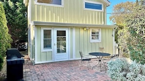 Ein zweistöckiges Haus mit einer Ziegelterrasse, einem Grill und einem kleinen Tisch mit Stühlen.