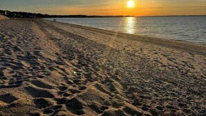 Ein Strand mit Fußspuren, die zum Wasser führen, einem Sonnenuntergang im Hintergrund und einem klaren Himmel.