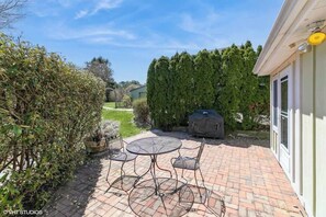 Une terrasse avec une table ronde et des chaises, un barbecue et une haie.