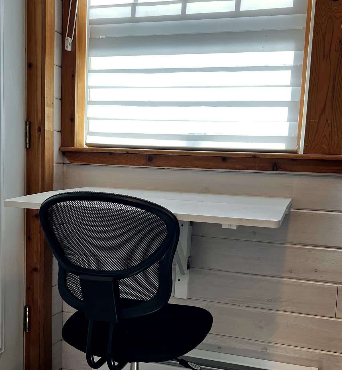 Ein Zimmer mit Fenster, einem Stuhl und einem weißen Regal.