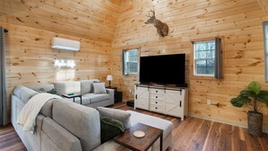 A log cabin interior with a sofa set, a television, a cabinet, and a mounted deer head. - Poplar Ridge | Hocking Hills, Sleeps 7, Hot Tub (McArthur)