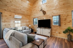 A log cabin interior with a sofa set, a television, a cabinet, and a mounted deer head. - Poplar Ridge | Hocking Hills, Sleeps 7, Hot Tub (McArthur)
