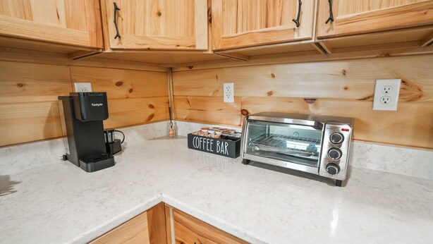 A kitchen with wooden cabinets, a coffee maker, a toaster, and a coffee bar sign. - Poplar Ridge | Hocking Hills, Sleeps 7, Hot Tub (McArthur)