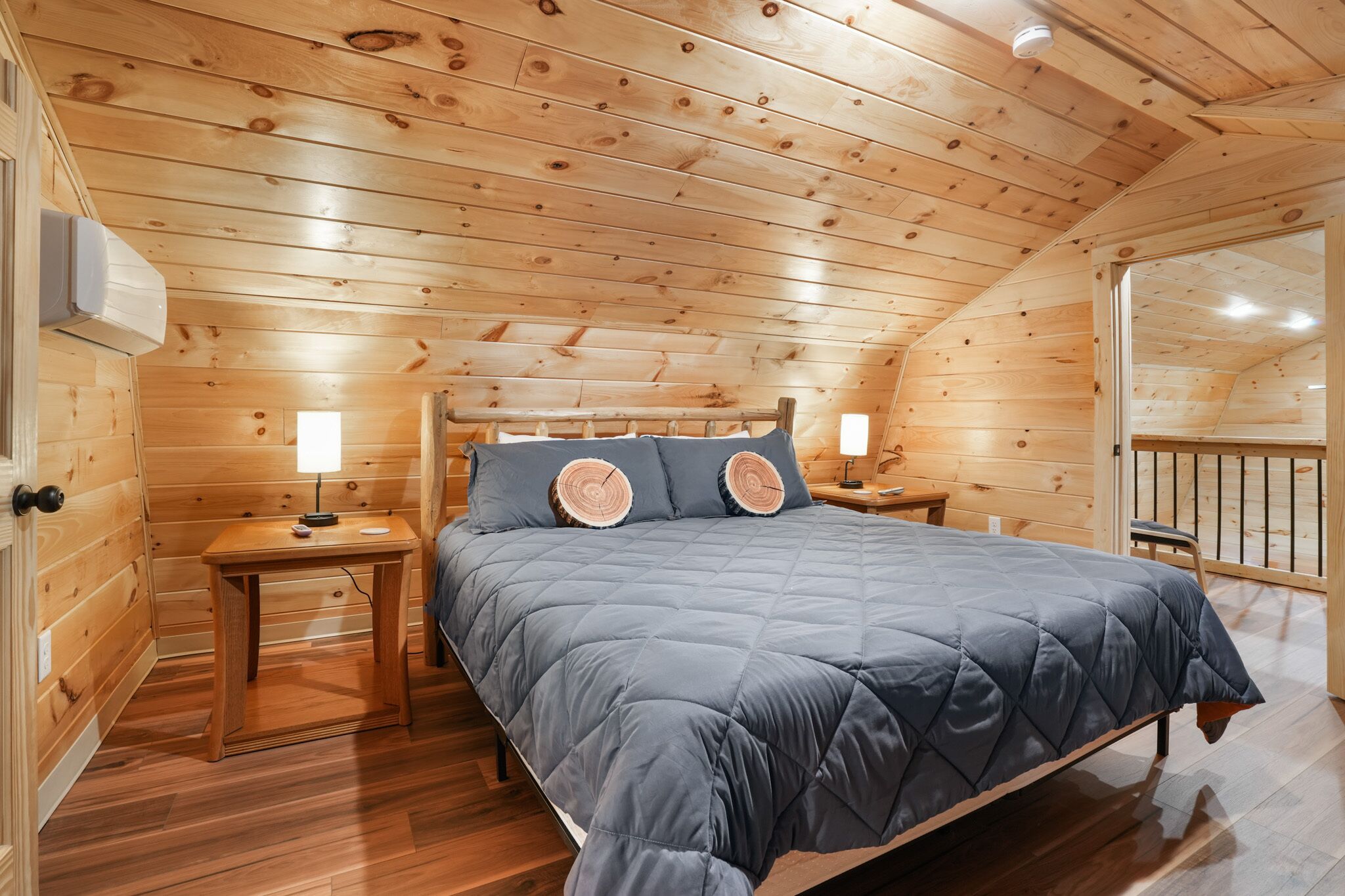 Un dormitorio rústico con cabaña de madera, una cama, mesitas de noche y una pequeña mesa con una lámpara.