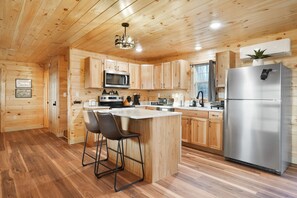 A modern kitchen with wooden cabinets, stainless steel appliances, and a bar area with stools. - Poplar Ridge | Hocking Hills, Sleeps 7, Hot Tub (McArthur)