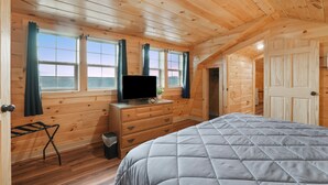 A wooden cabin bedroom with a bed, dresser, TV, and windows. - Poplar Ridge | Hocking Hills, Sleeps 7, Hot Tub (McArthur)