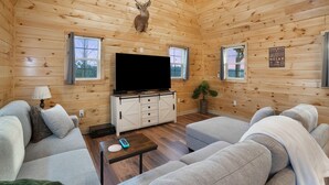 A log cabin interior with a mounted deer head, a television on a wooden cabinet, and a couch. - Poplar Ridge | Hocking Hills, Sleeps 7, Hot Tub (McArthur)