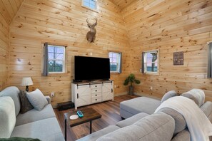 A log cabin interior with a mounted deer head, a television on a wooden cabinet, and a couch. - Poplar Ridge | Hocking Hills, Sleeps 7, Hot Tub (McArthur)