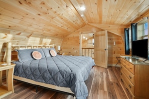 A cozy wooden cabin bedroom with a bed, dresser, and TV. - Poplar Ridge | Hocking Hills, Sleeps 7, Hot Tub (McArthur)