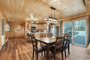A wooden cabin interior with a dining area, kitchen, and large sliding glass doors leading to a deck. - Poplar Ridge | Hocking Hills, Sleeps 7, Hot Tub (McArthur)