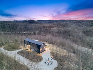 A modern cabin with a large deck and a fire pit, surrounded by a forested landscape. - Poplar Ridge | Hocking Hills, Sleeps 7, Hot Tub (McArthur)