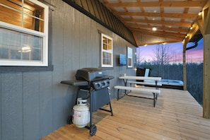 A covered outdoor area with a barbecue grill, a gas tank, and a picnic table.