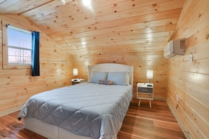 A wooden cabin bedroom with a bed, nightstands, and an air conditioning unit.